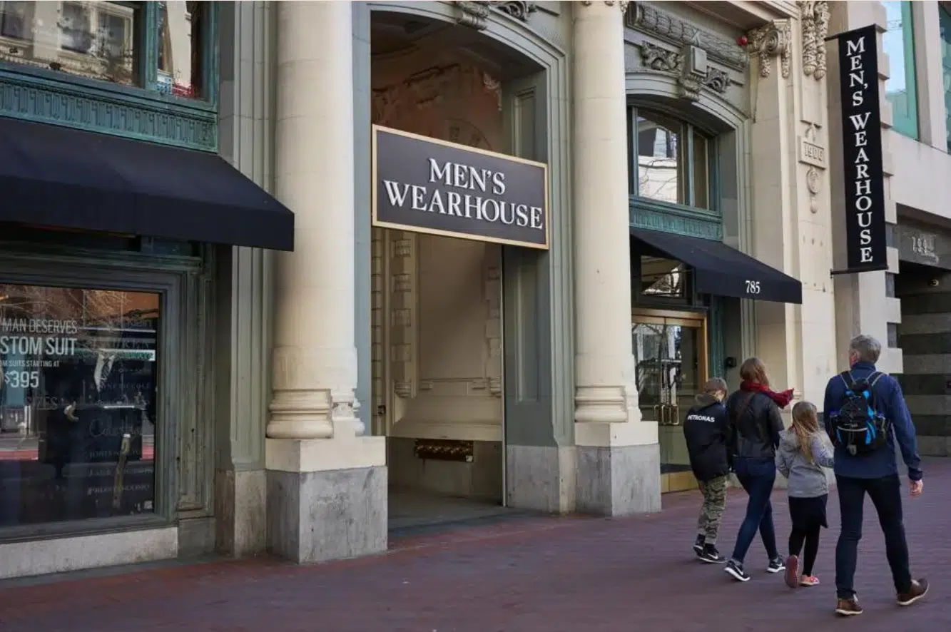 Three people walking in front of a Men's Wearhouse storefront